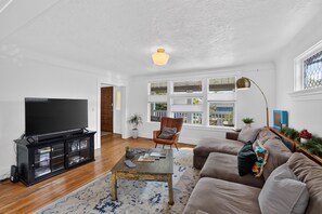 A living room with a flat-screen TV, a coffee table, a sofa, and a chair. - Inner Portland Craftsman | Hot Tub & Pool Table (Portland)