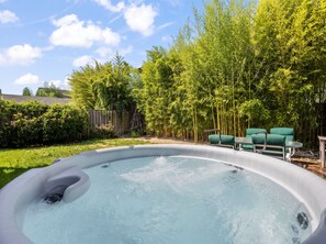 A hot tub with a wooden deck and green chairs, surrounded by bamboo and other greenery. - Inner Portland Craftsman | Hot Tub & Pool Table (Portland)