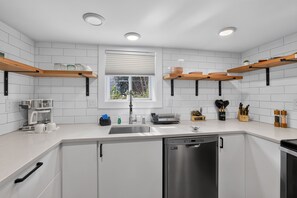 Eine moderne Küche mit weißen Schränken, Edelstahlgeräten und Holzregalen.