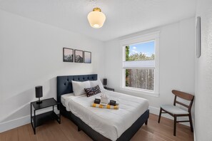A bedroom with a bed, a nightstand, a chair, a window, and wall art. - Inner Portland Craftsman | Hot Tub & Pool Table (Portland)