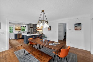 A modern kitchen with a central island, wooden dining table, and orange chairs. - Inner Portland Craftsman | Hot Tub & Pool Table (Portland)