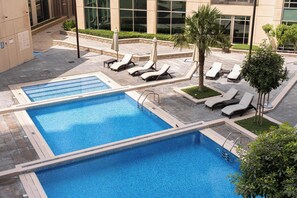 A rooftop pool area with multiple lounge chairs and a small table, surrounded by greenery and a building with large windows. - Free Housekeeping Visits During Your Stay - Stayshort - Modern and Chic Studio in Downtown With Burj Khalifa Views (Dubai)