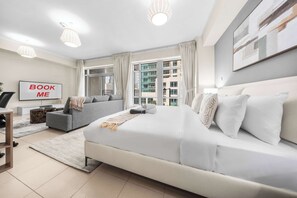A modern hotel room with a large bed, a sofa, a desk, and a television. - Free Housekeeping Visits During Your Stay - Stayshort - Modern and Chic Studio in Downtown With Burj Khalifa Views (Dubai)
