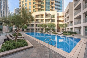 A swimming pool area with lounge chairs and a view of high-rise buildings. - Free Housekeeping Visits During Your Stay - Stayshort - Modern and Chic Studio in Downtown With Burj Khalifa Views (Dubai)