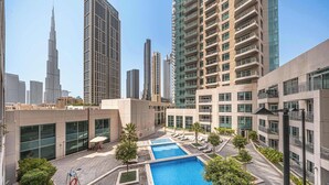 En modern bostadsbyggnad med ett poolområde på taket, omgiven av höga skyskrapor, inklusive Burj Khalifa.