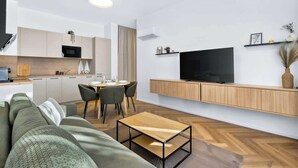 Ein modernes Wohnzimmer mit einer Couch, einem Couchtisch, einem Essbereich mit Stühlen, einer Küche mit Schränken und einem an der Wand montierten Fernseher.