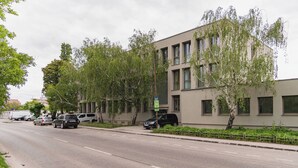 Ein modernes Gebäude mit flacher Fassade, zahlreichen Fenstern und einem Parkplatz mit Autos.