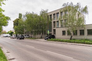 A modern building with a flat facade, multiple windows, and a parking area with cars. - Large Family Apartment for 6 - AC & Garage (Bratislava III)