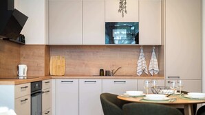 Eine moderne Küche mit weißen Schränken, einer Holz Arbeitsplatte, einem Einbauofen und einem Essbereich mit Tisch für Zwei.