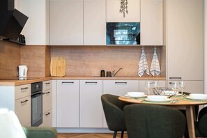 A modern kitchen with white cabinets, a wooden countertop, a built-in oven, and a dining area with a table set for two. - Large Family Apartment for 6 - AC & Garage (Bratislava III)