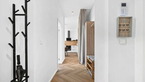 Ein Flur mit Kleiderhaken, Holzboden, einer in der Ferne liegenden Küchenzeile und einem an der Wand montierten Gegensprechanlage.