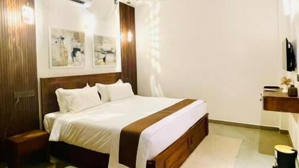 Un dormitorio con cama, ventilador de techo, mesita de noche y televisor montado en la pared, además de una ventana.