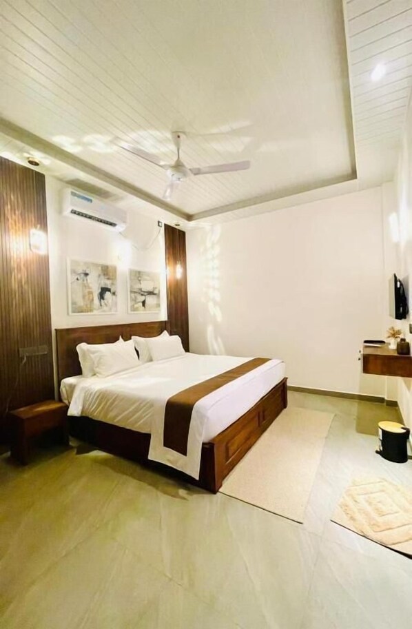 A bedroom with a bed, a ceiling fan, a bedside table, a nightstand, a wall-mounted TV, and a window. - Secret Gems Resort (Arugambay)