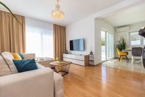 A modern living room with a sofa, a coffee table, a TV, and a dining area with a chair and a table. - Villa Astera with Privat Pool, 5 Bedrooms for 9 Guests, (Jesenice)