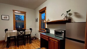 Cocina compacta con suelo de madera, una mesa de comedor con sillas, un refrigerador, un microondas y una ventana con vistas.