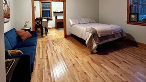 Un dormitorio con cama, piso de madera, ventilador de techo, ventana y puerta que da a un comedor.