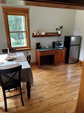 A kitchen with a dining table, chairs, a refrigerator, a microwave, and a window with a view of trees.