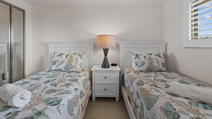 A bedroom with two beds, a nightstand with a lamp, and a window with blinds. - Carlos Pointe #213 Paradise Pointe (Fort Myers Beach)
