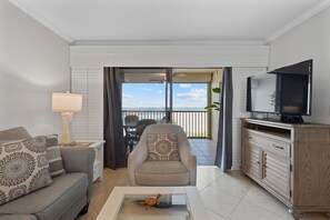 A living room with a sofa, armchair, coffee table, TV, and a balcony with a view. - Carlos Pointe #213 Paradise Pointe (Fort Myers Beach)