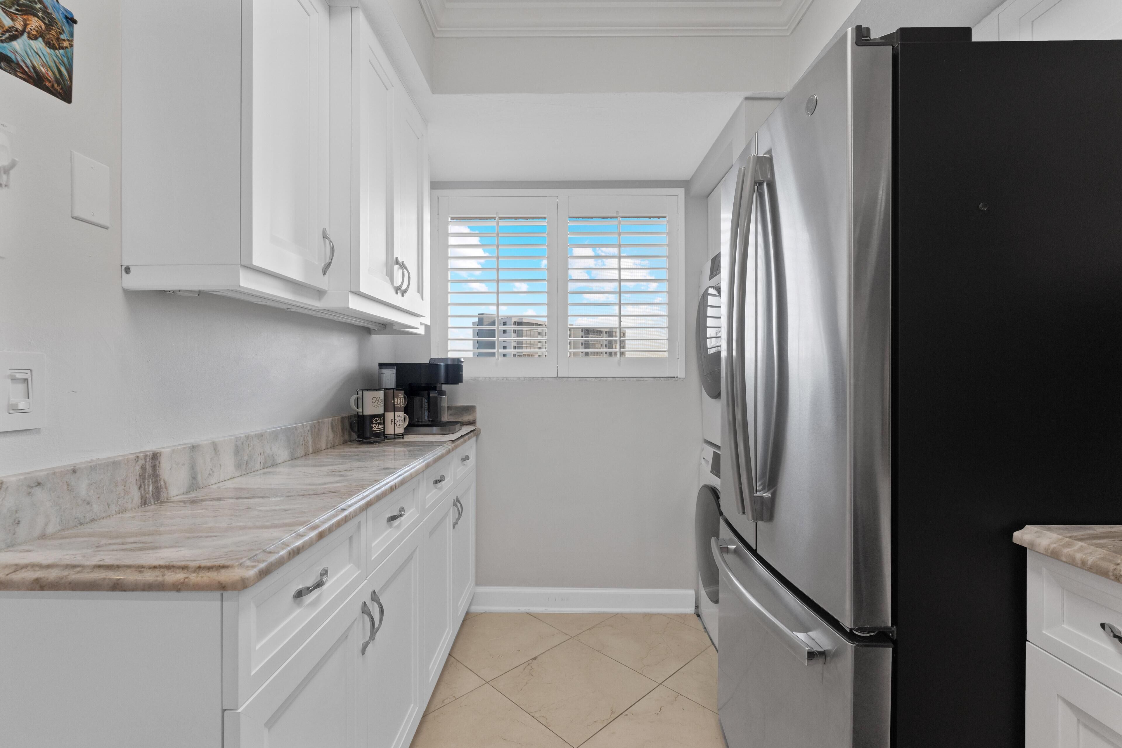 A kitchen with white cabinets, a black refrigerator, and a window with blinds.