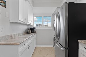 A kitchen with white cabinets, a black refrigerator, and a window with blinds. - Carlos Pointe #213 Paradise Pointe (Fort Myers Beach)