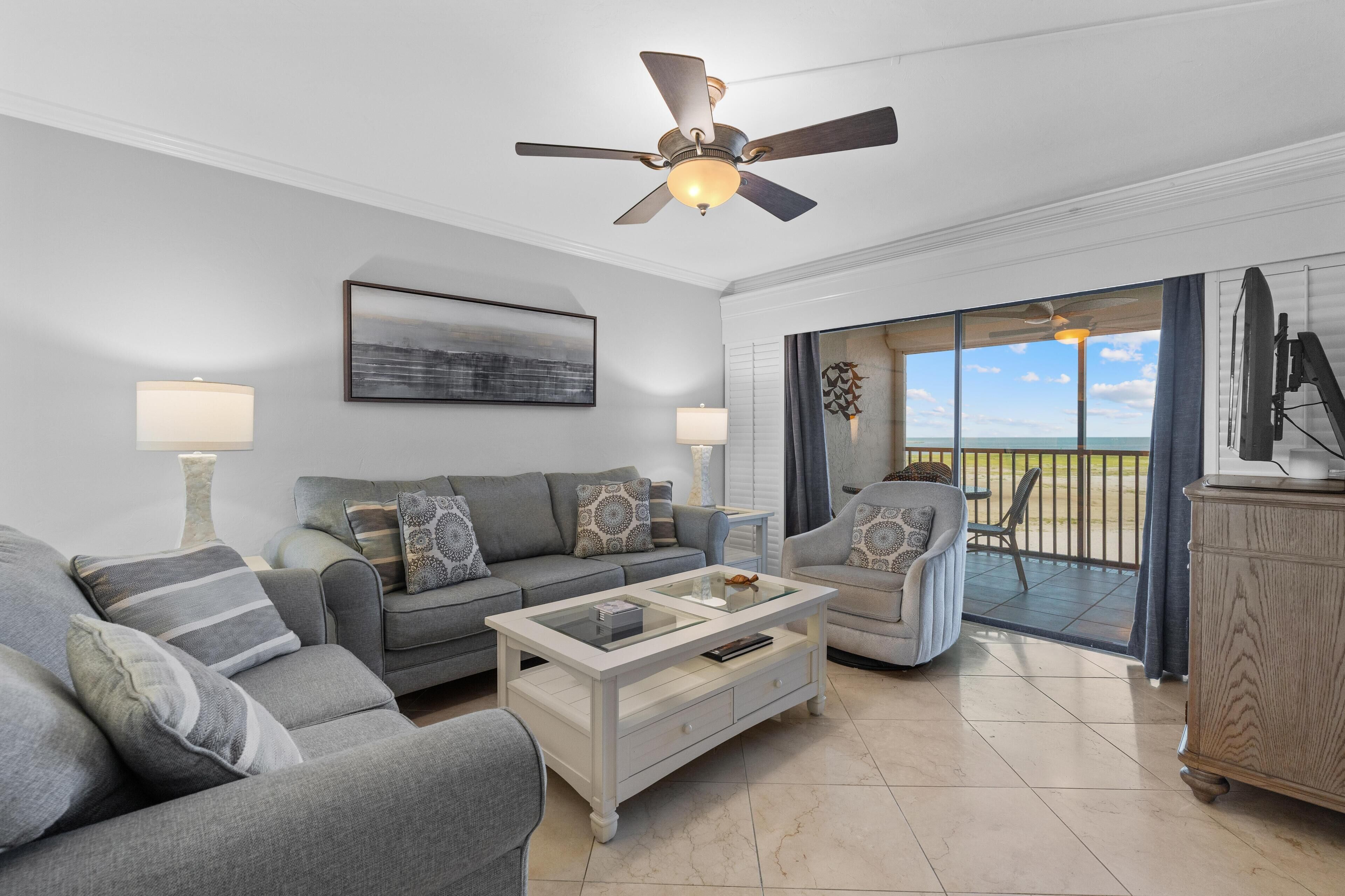 A modern living room with a ceiling fan, a large window with a view, and a dining area with a table and chairs.