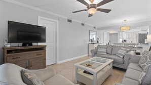 A modern living room with a flat-screen TV, a ceiling fan, a glass coffee table, and a grey sofa. - Carlos Pointe #213 Paradise Pointe (Fort Myers Beach)