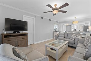 Ein modernes Wohnzimmer mit einem Flachbildfernseher, einem Deckenventilator, einem Glastisch und einem grauen Sofa.