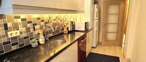 Una cocina moderna con encimera negra, armarios blancos y salpicadero de azulejos.