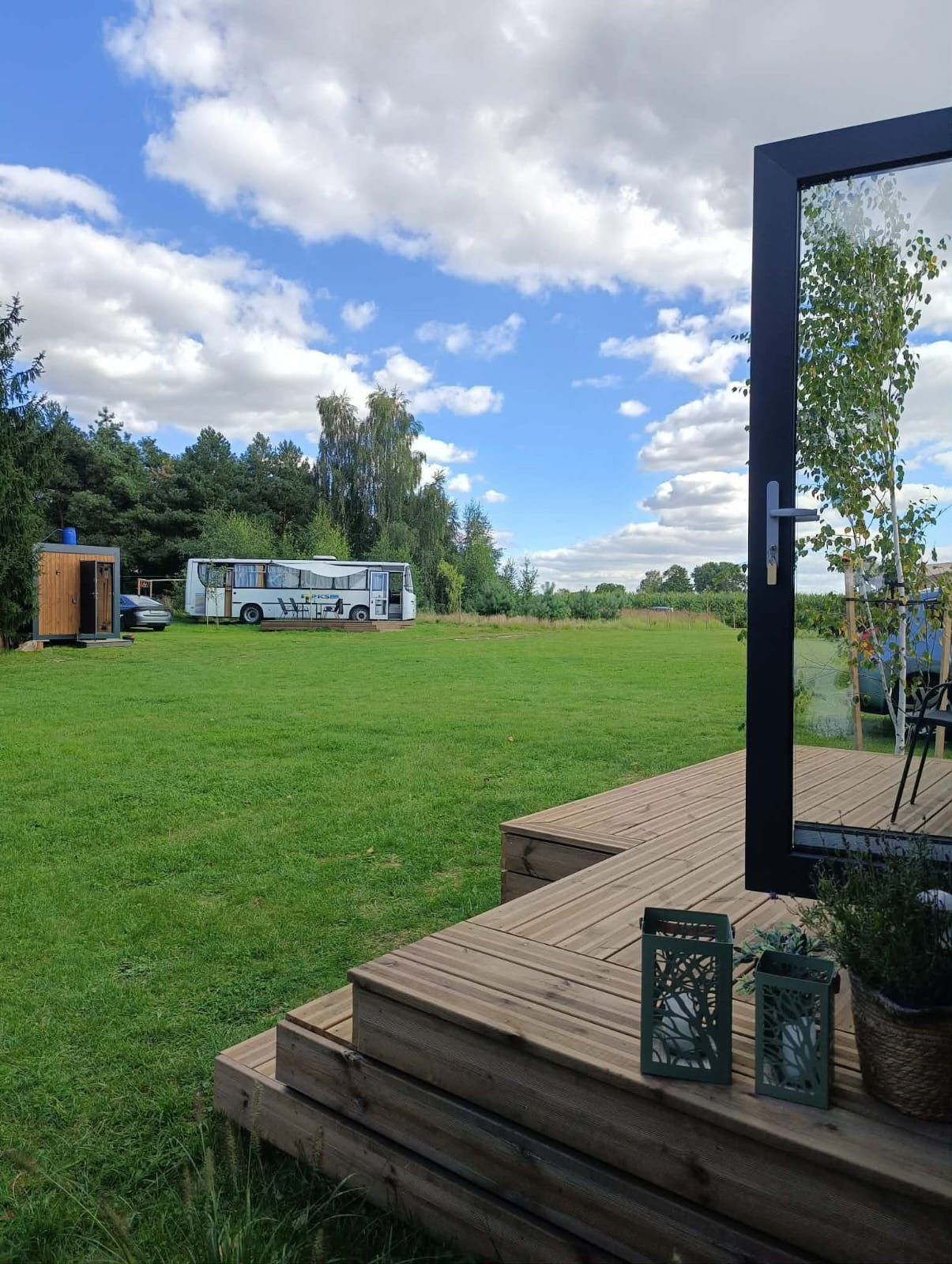 A grassy outdoor area with a wooden deck, a bus, and a small wooden structure.