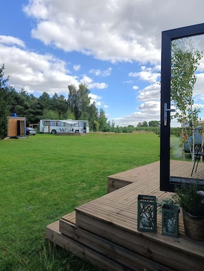 A grassy outdoor area with a wooden deck, a bus, and a small wooden structure.