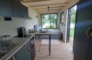 A modern kitchen with a dining area, large windows, and a view of greenery.