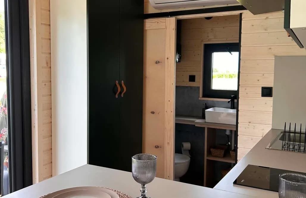 A modern interior with a wooden door leading to a bathroom, a white countertop, and a glass on the table.