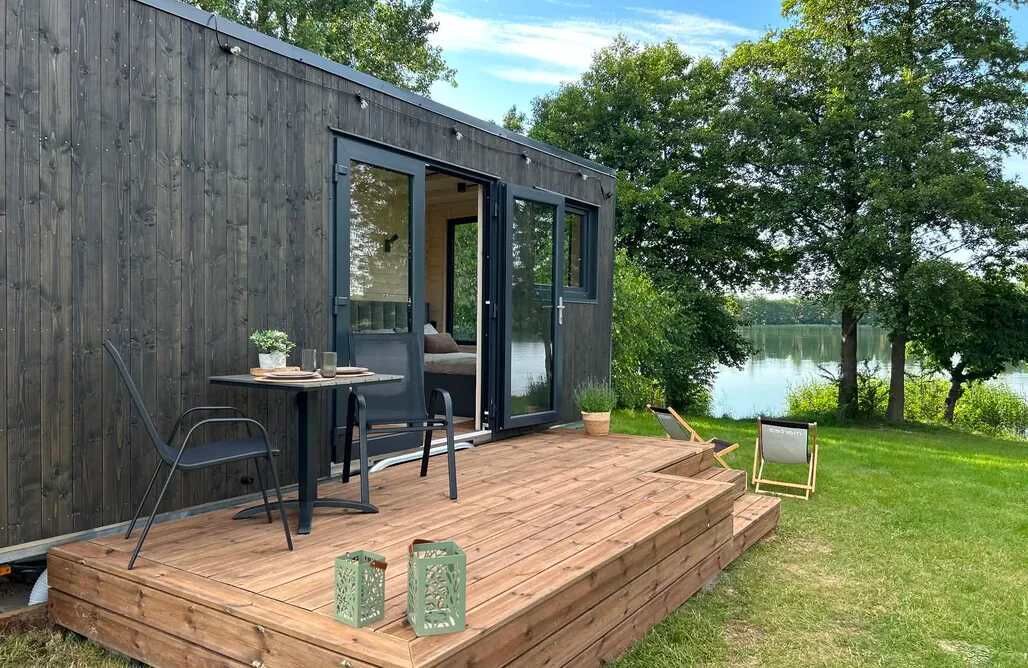 Une terrasse moderne en bois, avec une table et des chaises, donnant sur un lac.