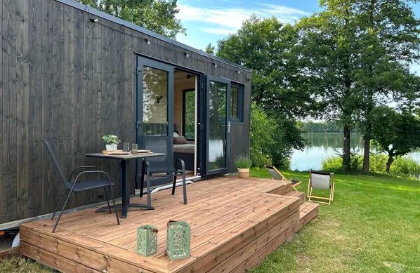 A modern wooden deck with a table and chairs, overlooking a lake.