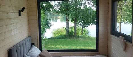 A room with a bed, a window, and a view of a lake and trees.