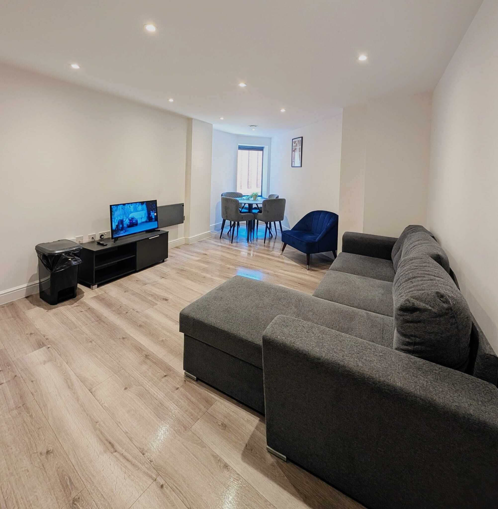 A modern living room with a large grey sectional sofa, a flat-screen TV, and a dining area with a table and chairs.