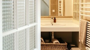 Un baño con suelo de madera, lavamanos blanco, espejo y toallero.