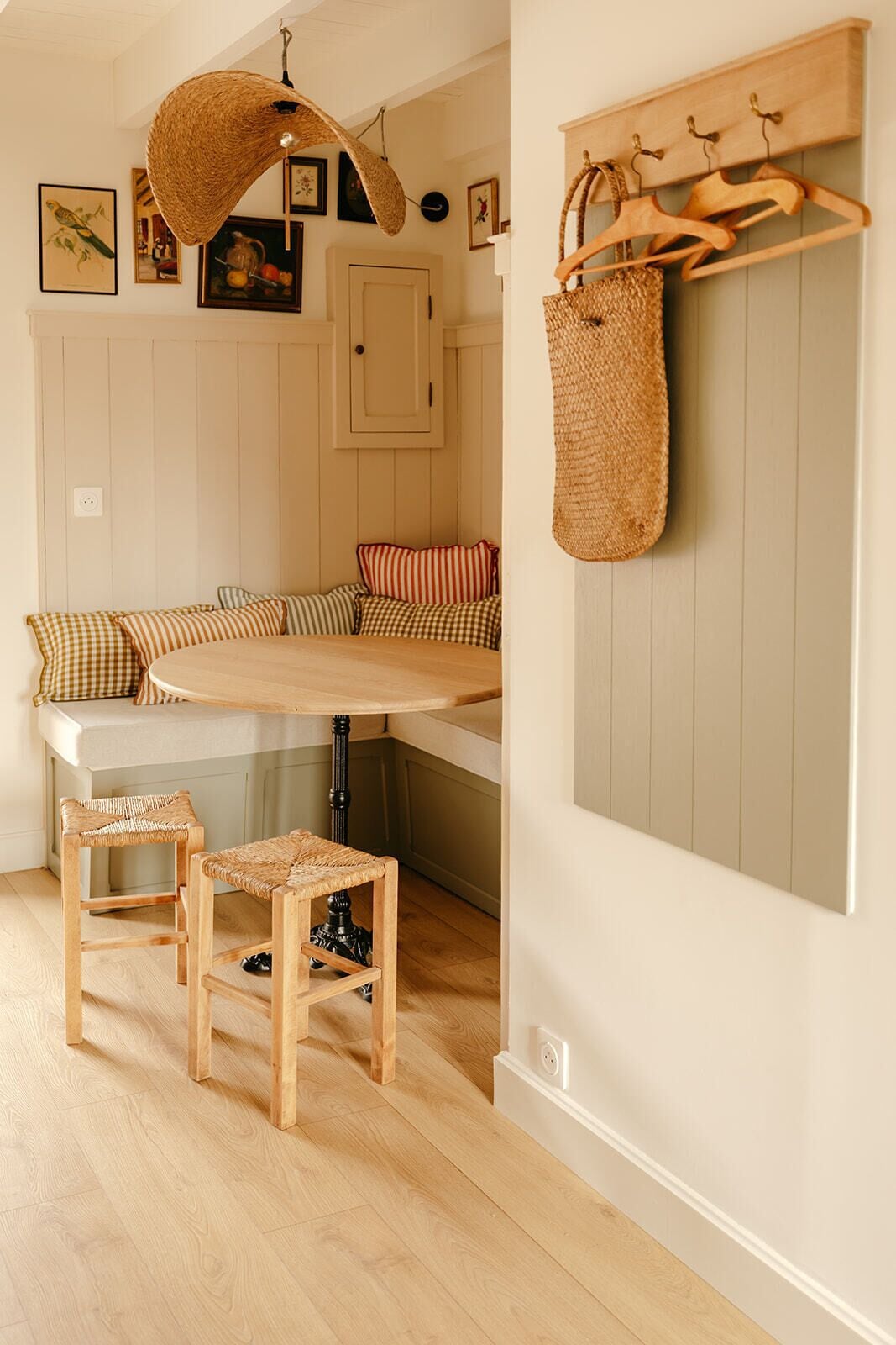 Una habitación acogedora con un banco empotrado, taburetes de madera, una cesta colgante tejida y un perchero.