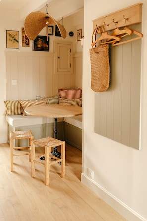 Una habitación acogedora con un banco empotrado, taburetes de madera, una cesta colgante tejida y un perchero.