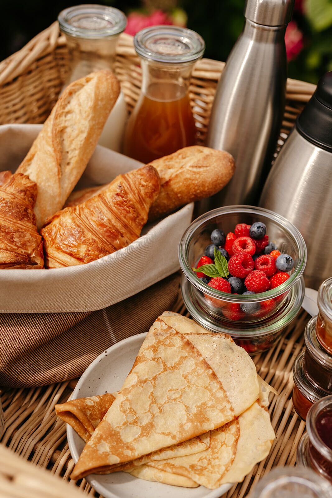 A wicker table with croissants, a bowl of berries, and a thermos.
