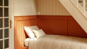 Een slaapkamer met een enkel bed, een houten vloer, een witte deur met raam en een trap met stenen muur.