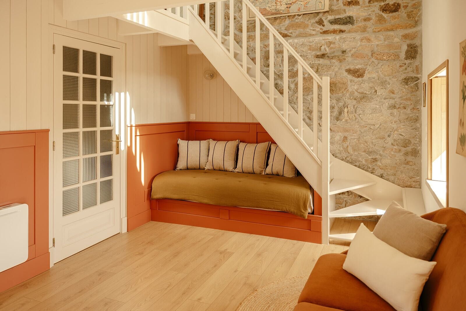 Una habitación con suelo de madera, una cama con cabecera marrón, una escalera blanca y una pared de piedra.