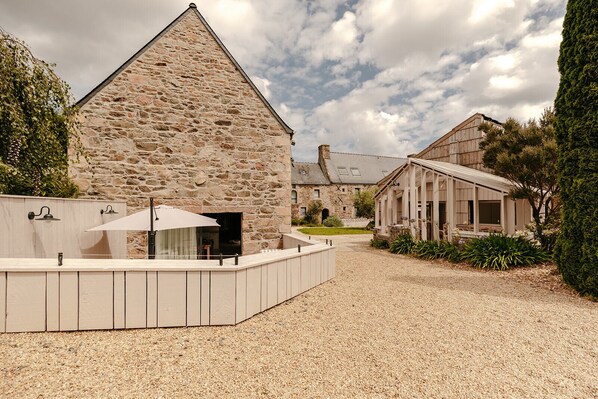 A stone building with a sloped roof, a gravel driveway, and a wooden structure with a porch.