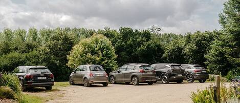 A gravel parking area with several cars parked, surrounded by greenery and trees.