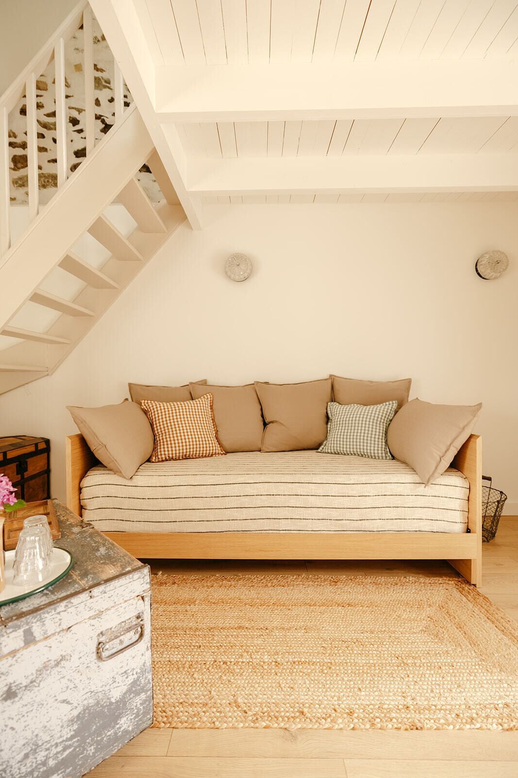 Un salon chaleureux avec un canapé, un tapis tissé, une malle en bois et un escalier.