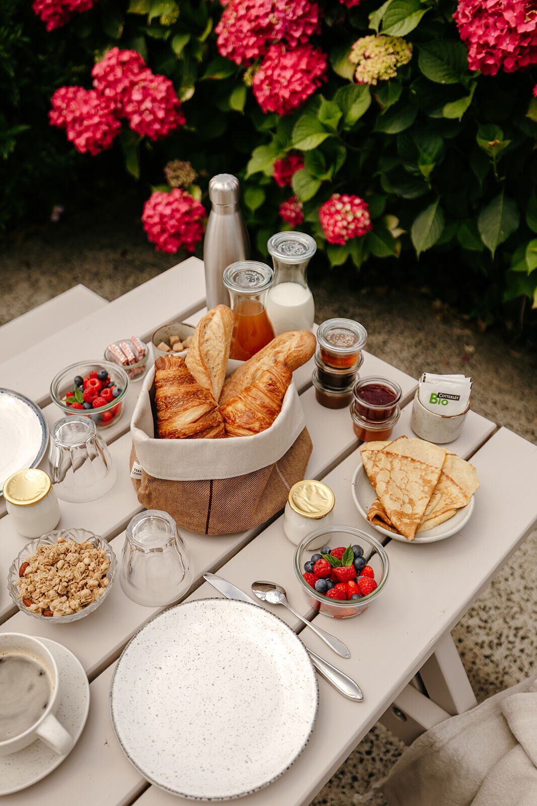 Un pique-nique avec du pain, des baies et des condiments, le tout disposé sur une table à l’extérieur.