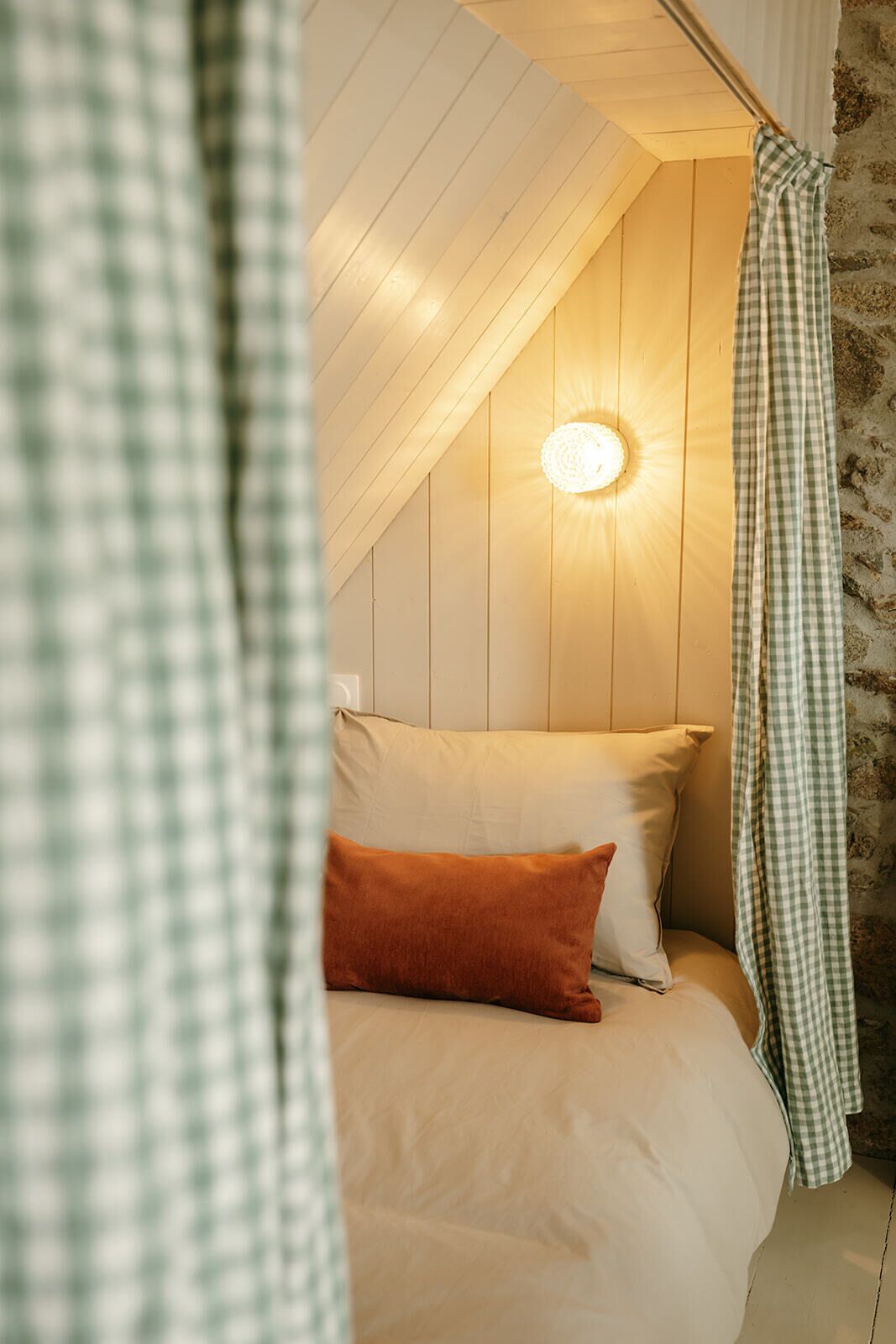 A cozy room with a bed, a hanging light fixture, and a checkered curtain.
