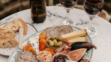 A charcuterie board with various meats, cheeses, and fruits, accompanied by two glasses of red wine, on a marble table.
