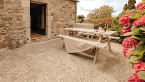 Un edificio de piedra con un banco de madera y una mesa de picnic, una puerta y una ventana.